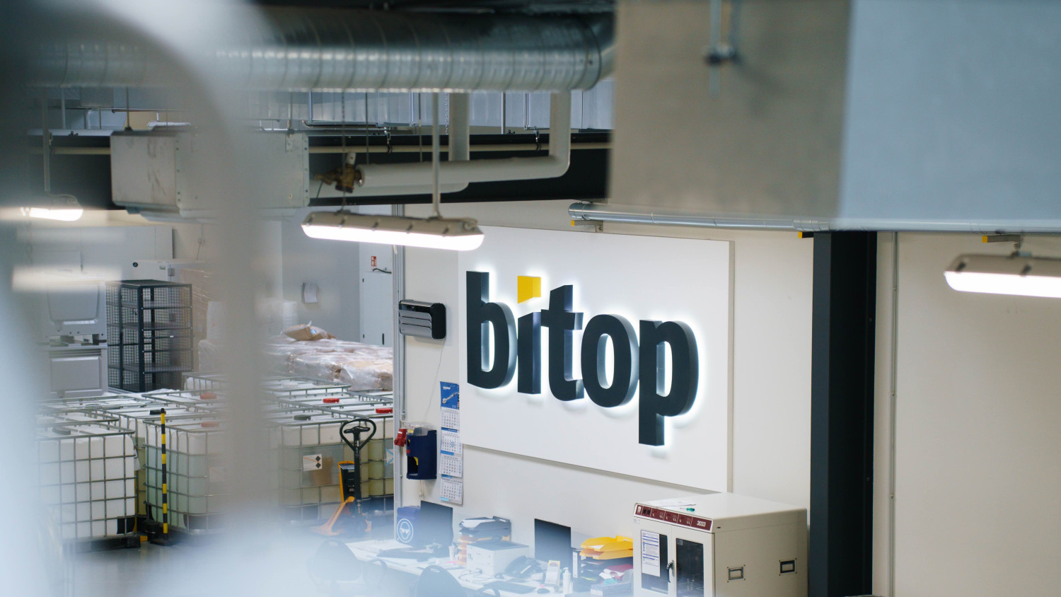 Arbeitsplatz in einer technischen Halle mit einem großen bitop-Logo über dem Schreibtisch